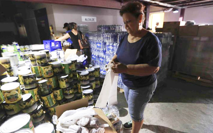 Morovis, Puerto Rico. Preparando cajas y bolsas de suministros básicos para los habitantes de barrios lejos del pueblo. Durante los primeros días después del embate del huracán María, escaseaban agua y alimentos. Luego, poco a poco aumentaban las entregas de estos artículos de primera necesidad. Las facilidades del gobierno municipal fueron convertidas en almacenes donde trabajan voluntarios en la preparación y repartición de lo traído por helicópteros y camiones, echado a un lado lo de politiquería. 